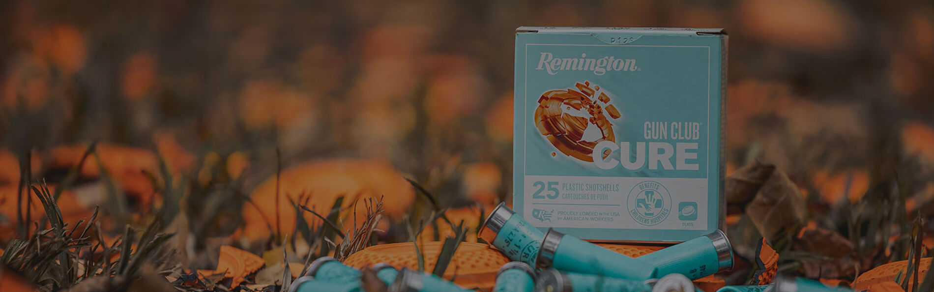 Remington Gun Club Cure box and shotshell sitting in the grass with broken clays