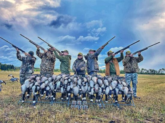 hunters aiming shotguns in front of dead geese